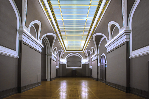 Salle avec arches, plancher en bois et éclairage au plafond.