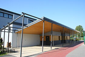 Bâtiment avec structure métallique, véranda, porte vitrée, allée et trottoir.