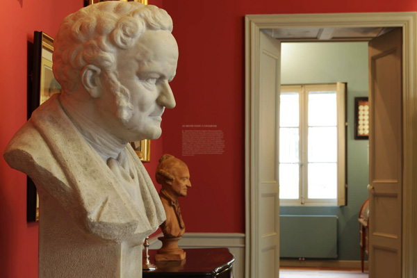 Salle avec buste en marbre, porte, tableau, et canapé visible à travers la porte.