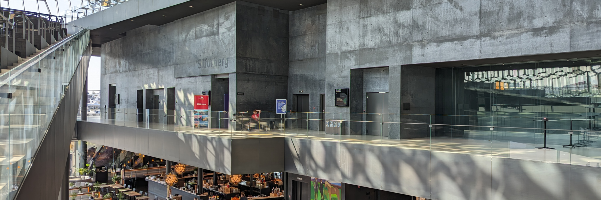Bâtiment moderne avec escalier, balustrades en verre, espace ouvert, tables et chaises.