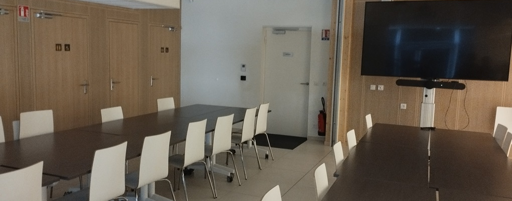 Salle avec tables, chaises, écran et porte.