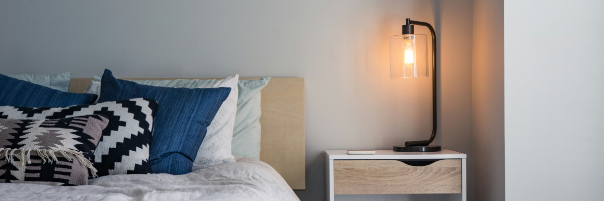 "Chambre avec lit, table de chevet, lampe et coussins".