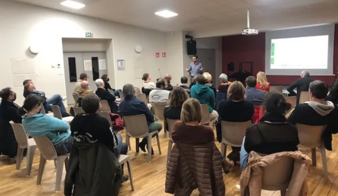 Salle de conférence avec public, chaises, écran, projecteur et intervenant.