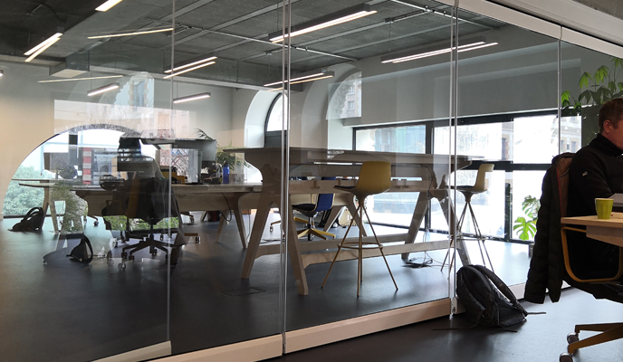 Espace de travail avec tables, chaises, ordinateurs, lampes et plantes.