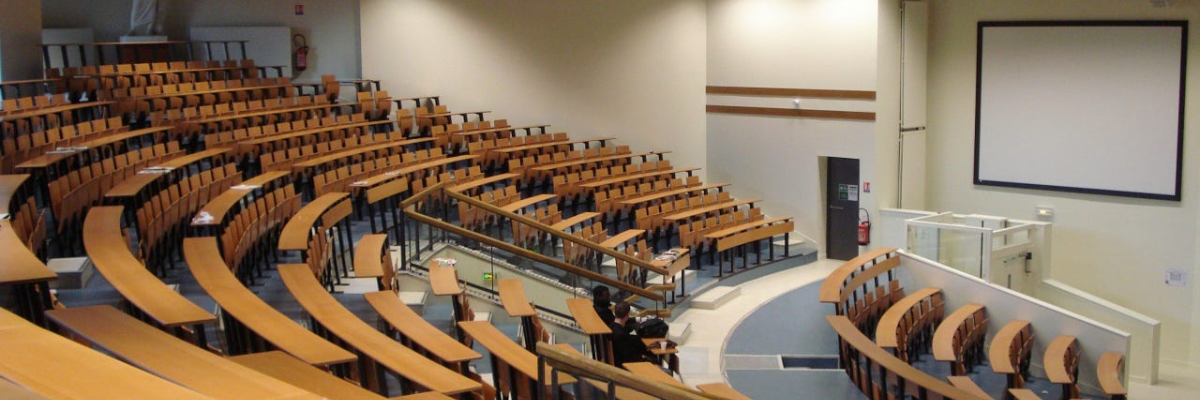Amphithéâtre avec gradins, chaises, table au centre, écran et projecteur.