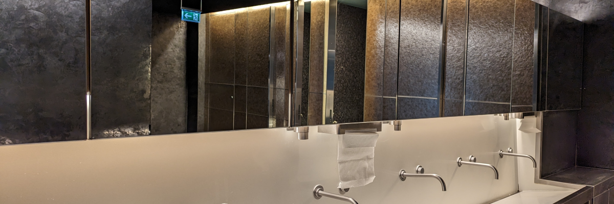 Lavabos alignés avec robinetterie, miroirs et éclairage mural.