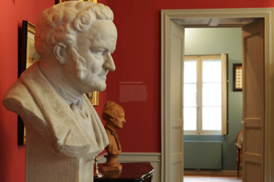 Salle avec buste en marbre, porte, tableau, et canapé visible à travers la porte.