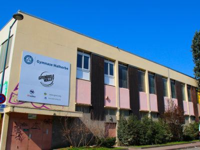 Gymnase avec panneaux d'affichage, fenêtres et végétation.