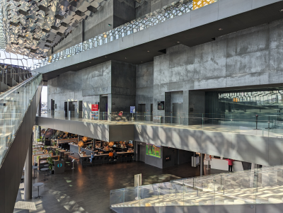 Bâtiment moderne avec escalier, balustrades en verre, espace ouvert, tables et chaises.