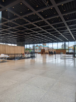 Grand espace avec plafond à panneaux, grandes fenêtres, escaliers, et tables.