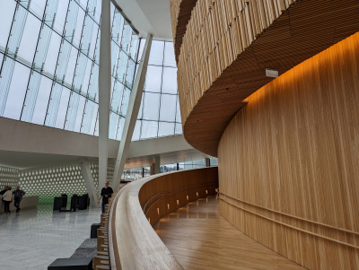 Espace moderne avec rampes en bois, murs en verre, et quelques personnes.