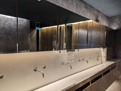 Lavabos alignés avec robinetterie, miroirs et éclairage mural.